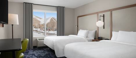 A hotel room with two beds, a desk, a chair, a TV, and a window with a view of mountains.