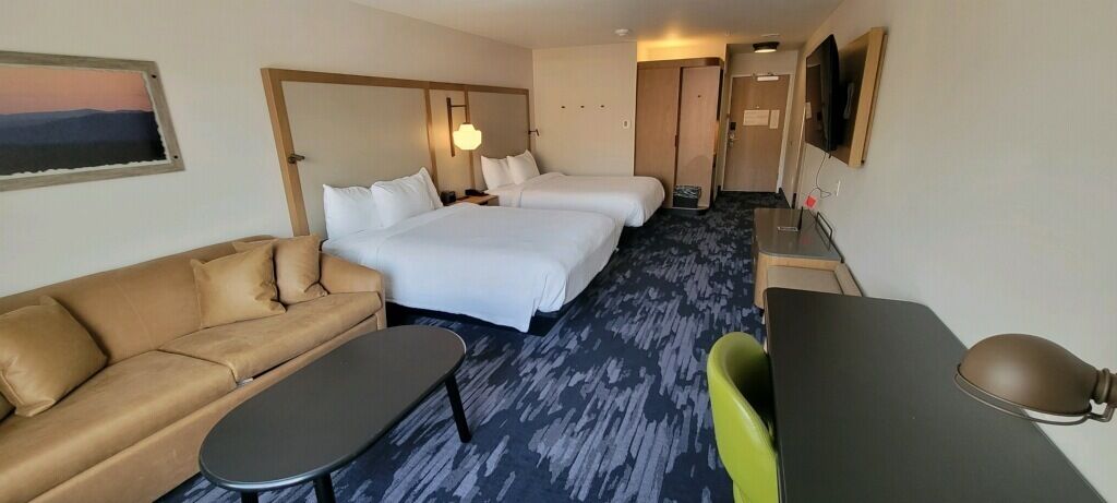 A hotel room with two beds, a sofa, a desk, a chair, and a TV.