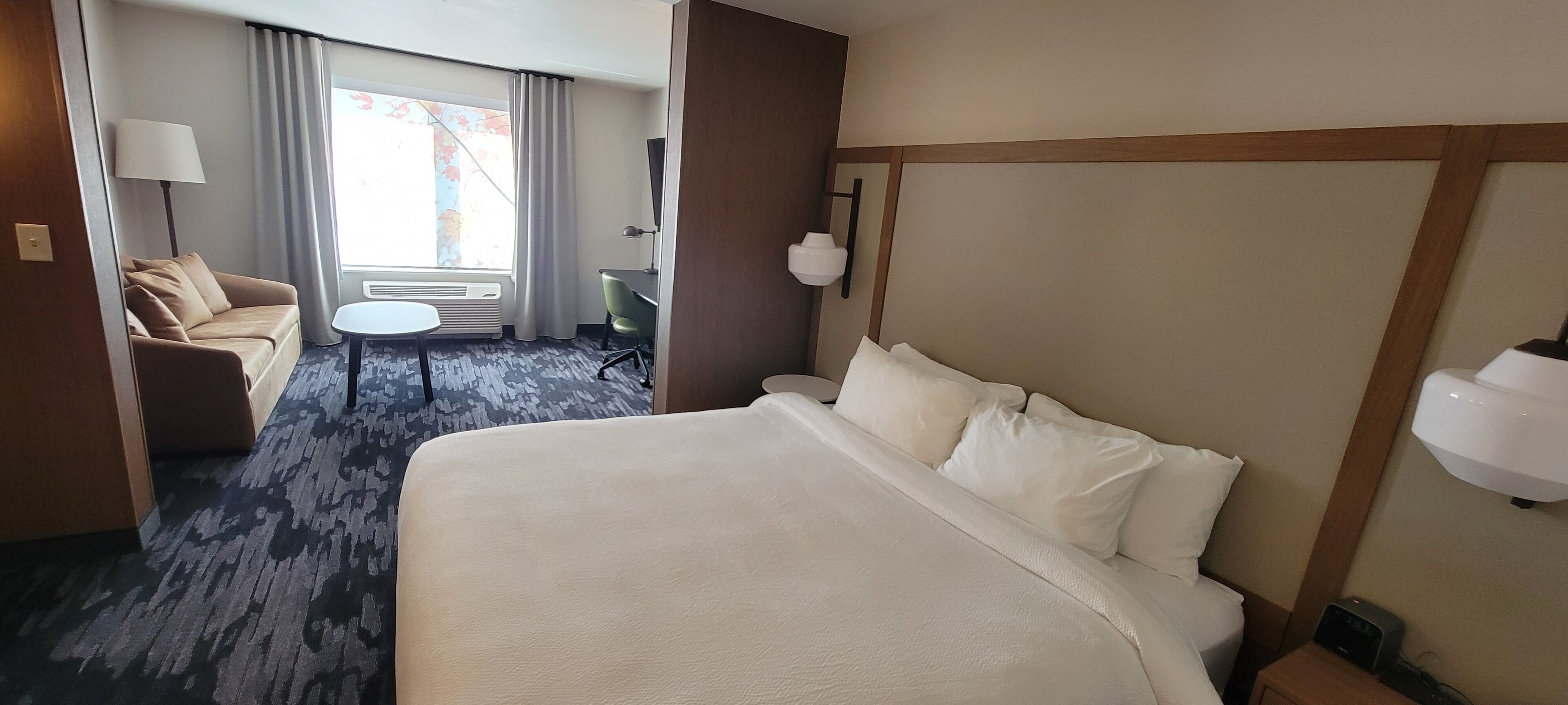 A hotel room with a large bed, a sofa, a small table, and a desk.