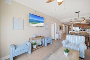 A spacious living area with a large flat-screen TV, a sofa, a coffee table, and a dining area with wooden furniture.