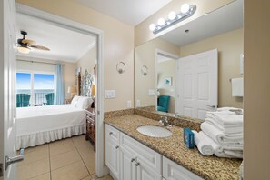 A hotel room with a bed, a bathroom with a sink and mirror, and a view of the ocean through a window.
