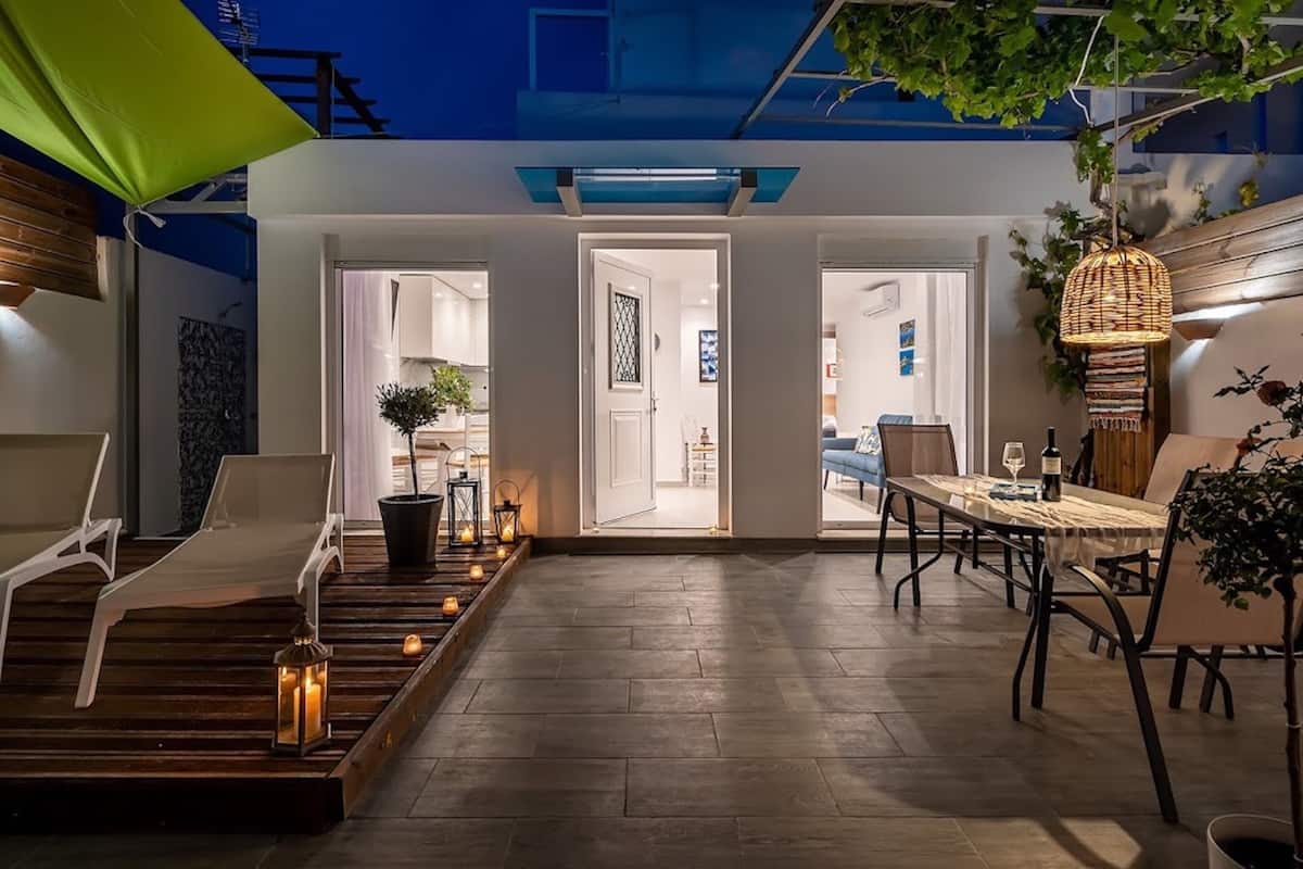 Un espace de vie extérieur moderne comprenant une table et des chaises de salle à manger, un fauteuil de détente et un petit coin jardin agrémenté de bougies.