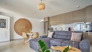 Een moderne woonkamer met een grijze modulaire bank, een rond geweven wanddecoratie en een eethoek met een witte tafel en stoelen.