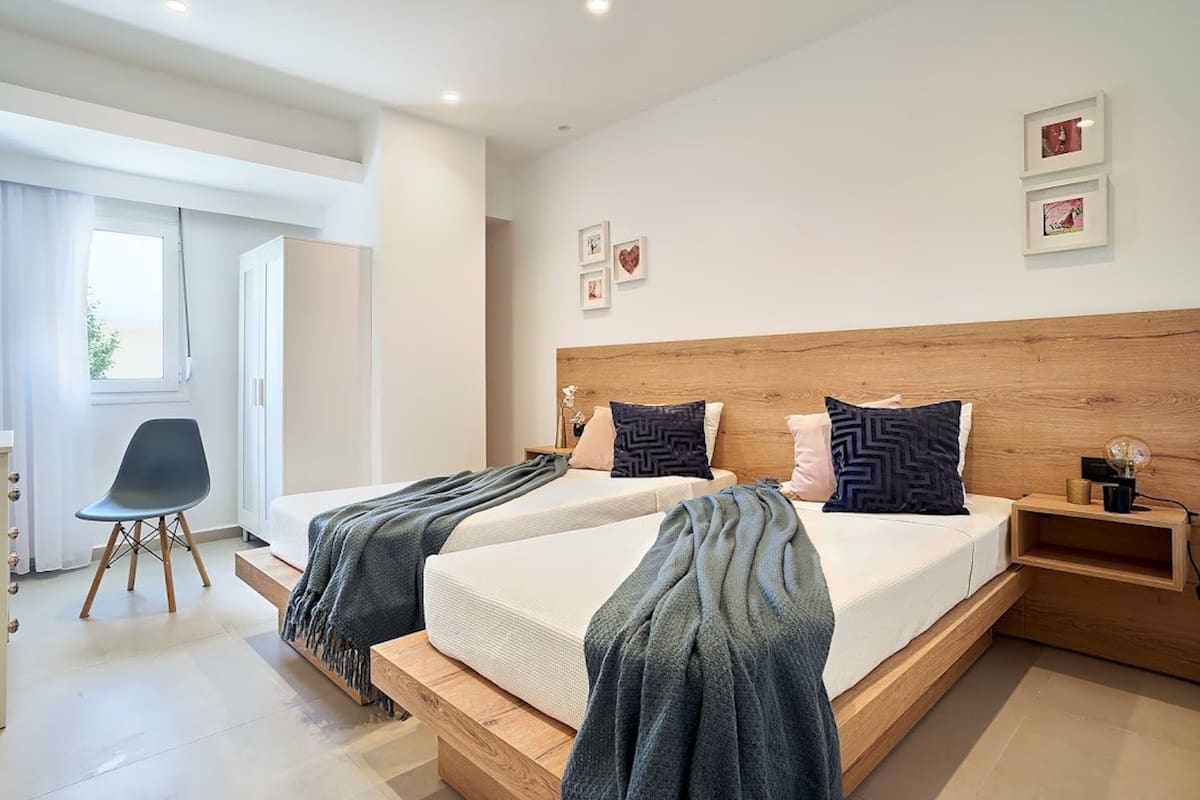 Une chambre moderne avec deux lits, une tête de lit en bois, des tables de chevet et une chaise.