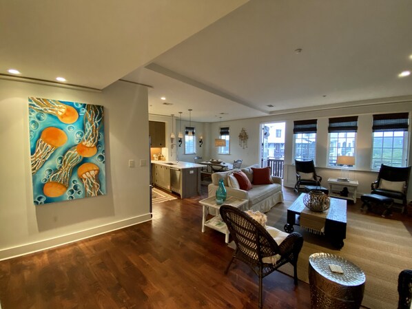 Amplia sala de estar con piso de madera, cocina con isla central y comedor con mesa y sillas.