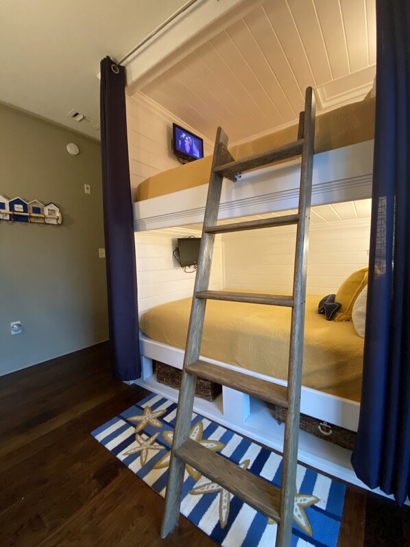A bunk bed with a wooden ladder, a television on the wall, and a starfish-patterned rug.