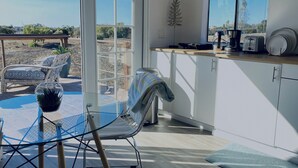 A modern kitchen with a glass table, chairs, and a view of the outdoors.