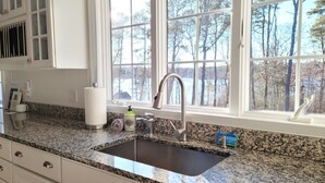 Una cocina con encimera de granito, pileta de acero inoxidable y ventana con vista a árboles.