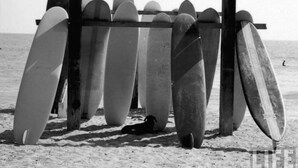 Een houten standaard met meerdere surfplanken op een zandstrand.