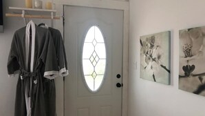 Een kamer met een witte deur, een badjas aan een rek en twee bloemschilderijen aan de muur.