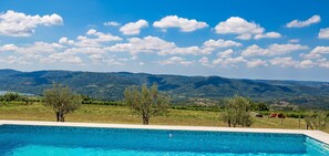 A clear blue swimming pool with a view of mountains and trees in the background.