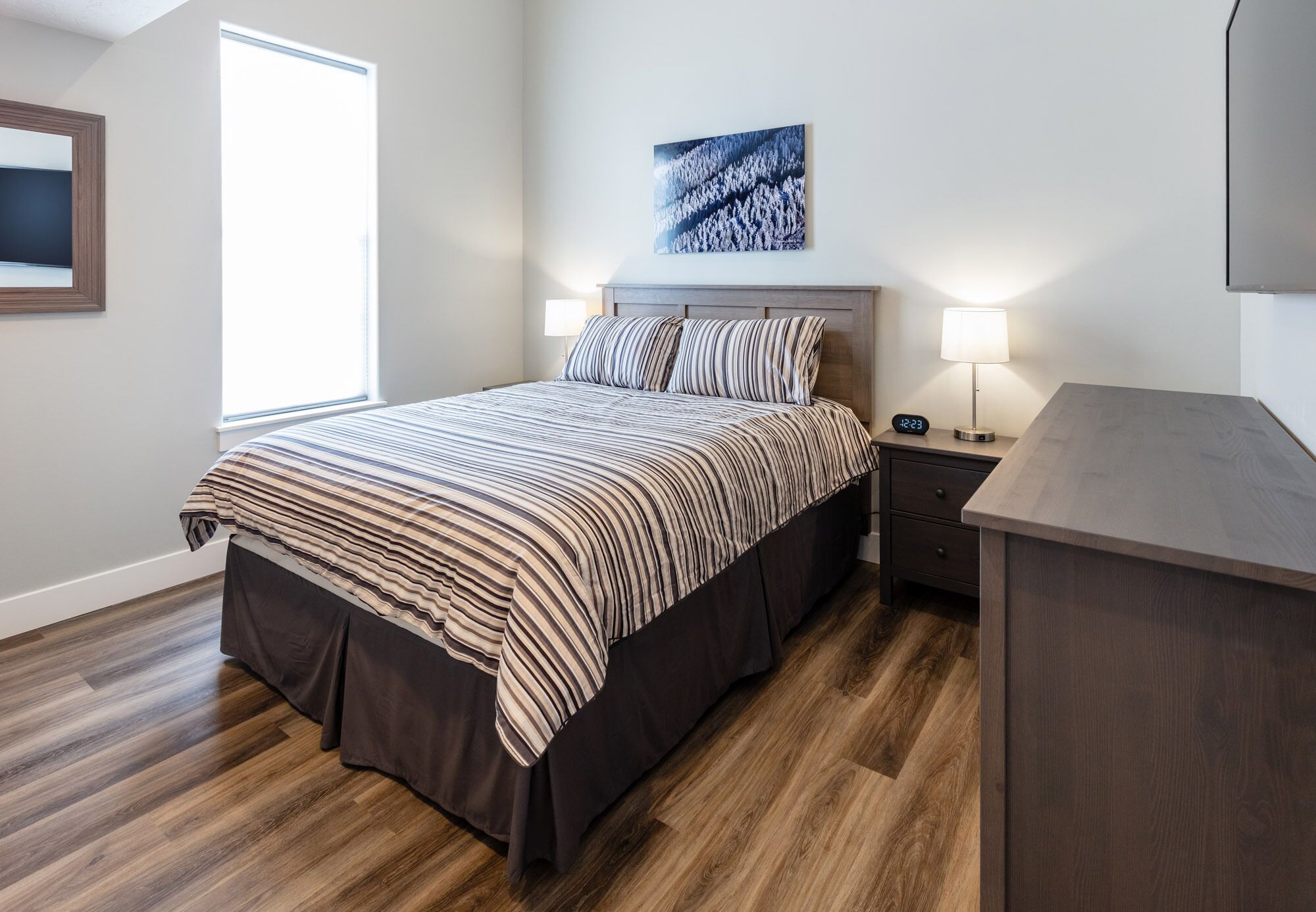 A bedroom with a large bed, a nightstand, a desk, and a window.