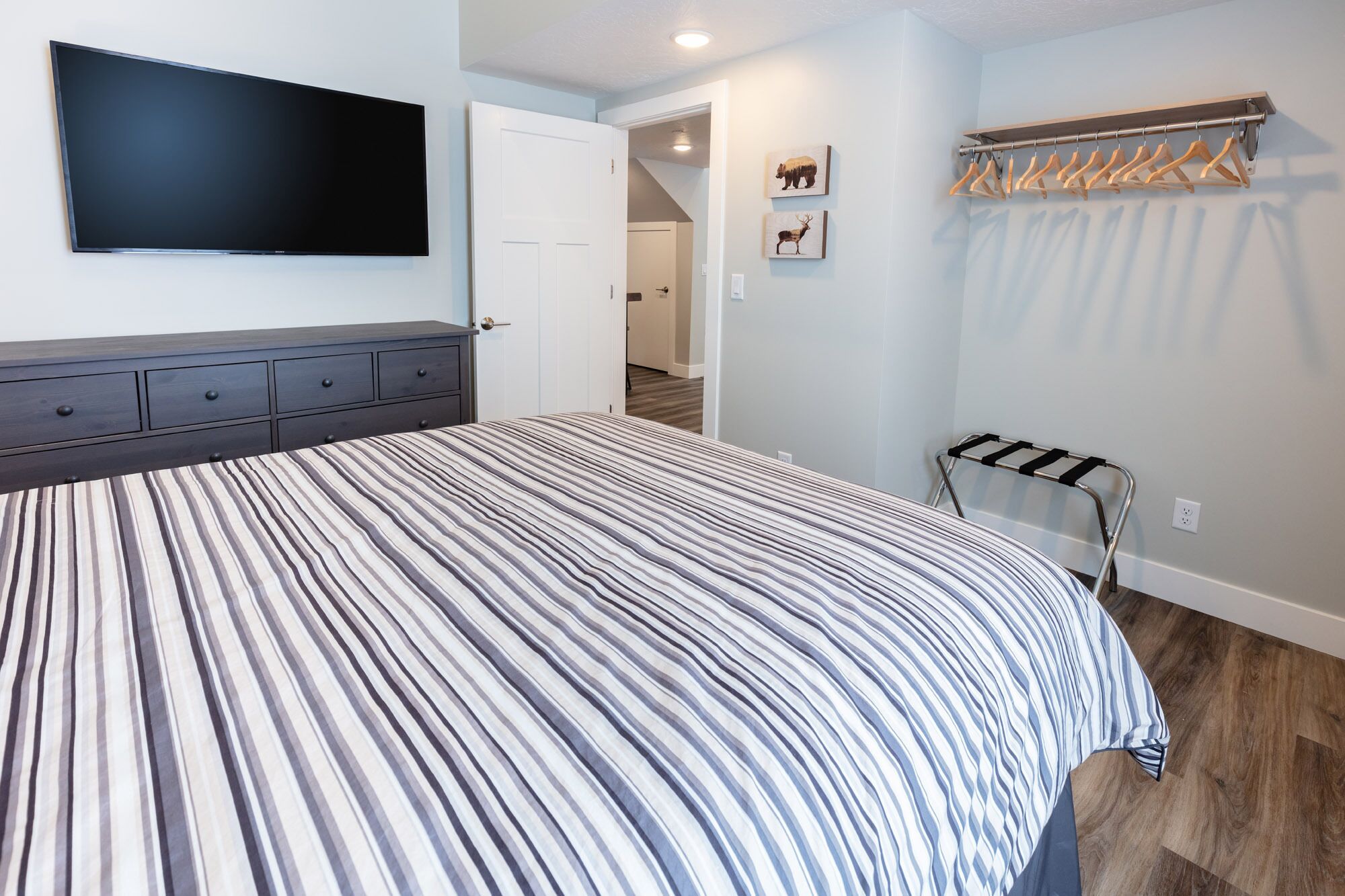 Une chambre à coucher comprenant un lit, un téléviseur, un porte-manteau et une porte donnant sur une autre pièce.