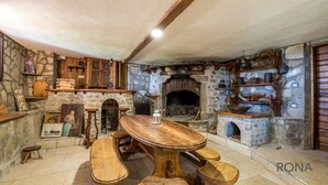 Ein rustikaler Raum mit Steinwänden, einem Holztisch, Bänken, einem Kamin und Regalen mit Keramik.