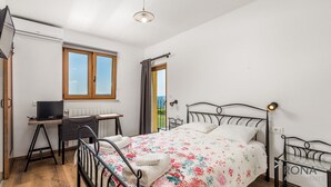 Ein Schlafzimmer mit Bett, Schreibtisch und Computer. Es gibt ein Fenster mit Vorhängen, eine Heizung und einen Blick ins Freie.