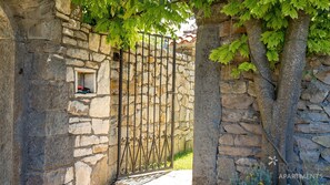 Secure entrance to RONA APARTMENTS, featuring a traditional metal gate and lush green surroundings.