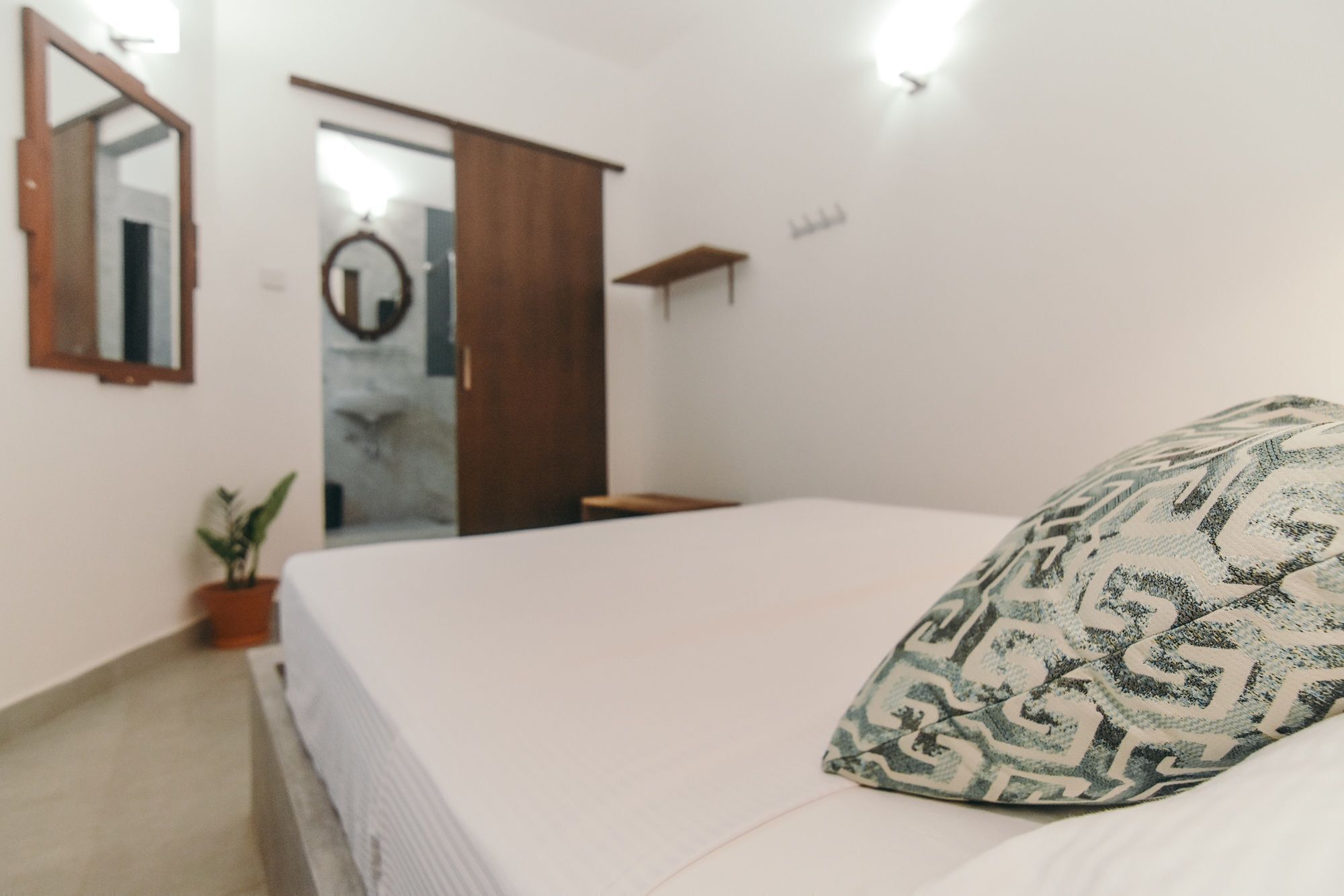 A bedroom with a bed, a mirror, a door, and a small plant.