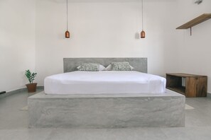 A minimalist bedroom with a large bed, two pendant lights, a small plant, and a wooden nightstand. - City Beds The Regent (Colombo)