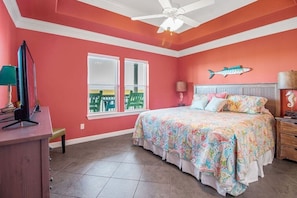 A bedroom with a large bed, a ceiling fan, a desk with a computer, and a window with a view of a green deck. - Gorgeous Home w/ Sargent Beach/ICW Views (Sargent)