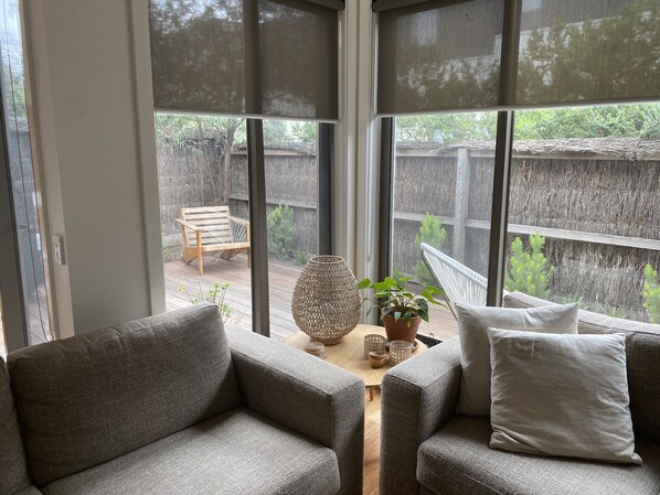 Relax in this inviting living area with a sofa, coffee table, and potted plant, offering a view of the backyard with a deck and chair.