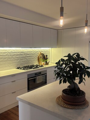 Una cocina moderna con armarios blancos, estufa a gas, horno empotrado y una planta en una maceta sobre la isla.