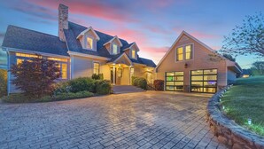 A two-story house with a brick driveway, a large garage, and a well-lit entrance. - 6BR/4.5BR Retreat: Views, Pool, HotTub, Sauna & Game-room (Leicester)