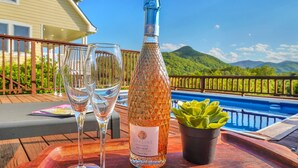 A bottle of Opaline Pinot Noir on a wooden table with two glasses and a succulent plant, overlooking a pool and mountains. - 6BR/4.5BR Retreat: Views, Pool, HotTub, Sauna & Game-room (Leicester)