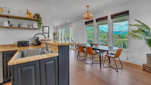 A modern kitchen with a central island, wooden shelves, and a dining area with a view of the outdoors. - 6BR/4.5BR Retreat: Views, Pool, HotTub, Sauna & Game-room (Leicester)