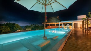 A nighttime swimming pool area with a wooden deck and a large umbrella providing shade.