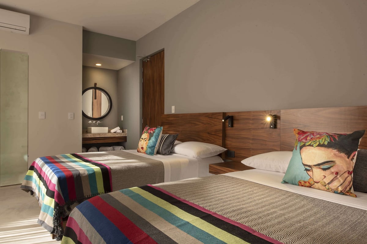 A hotel room with two beds, a wooden headboard, a mirror, and a bathroom with a sink and towel rack.