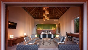 A spacious room with a high ceiling, a bed with a green headboard, a dining area, and a seating area with patterned chairs.