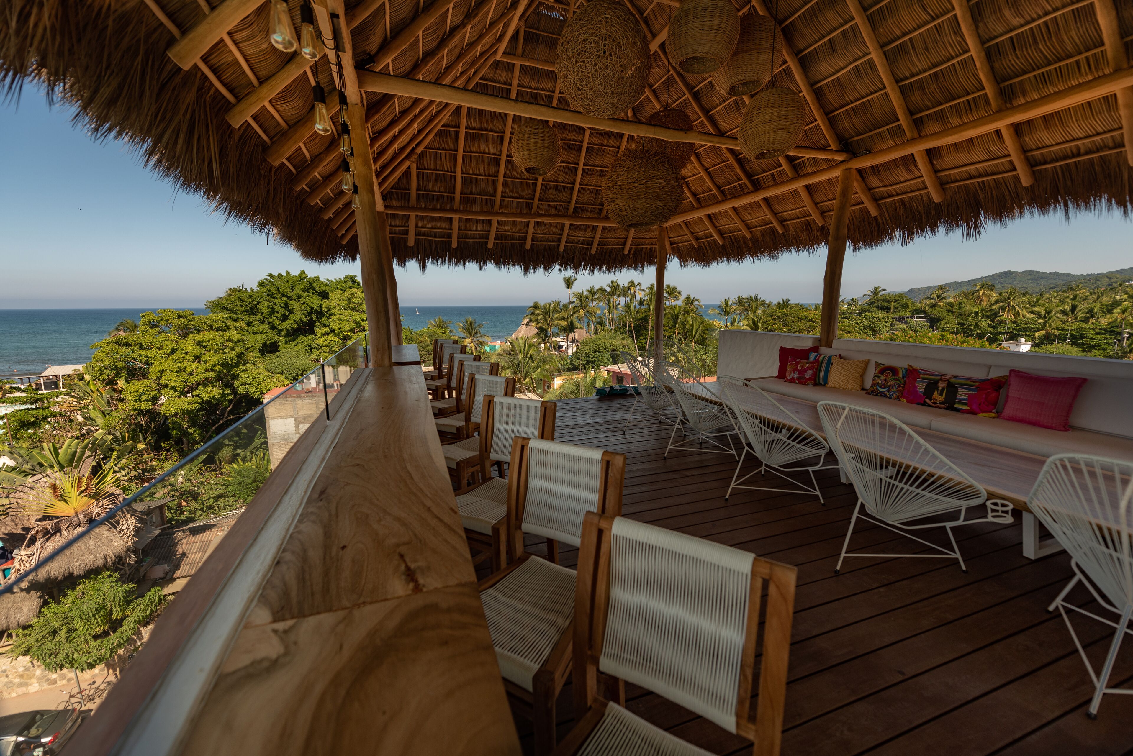 A wooden deck with white chairs and a thatched roof overlooking the ocean.