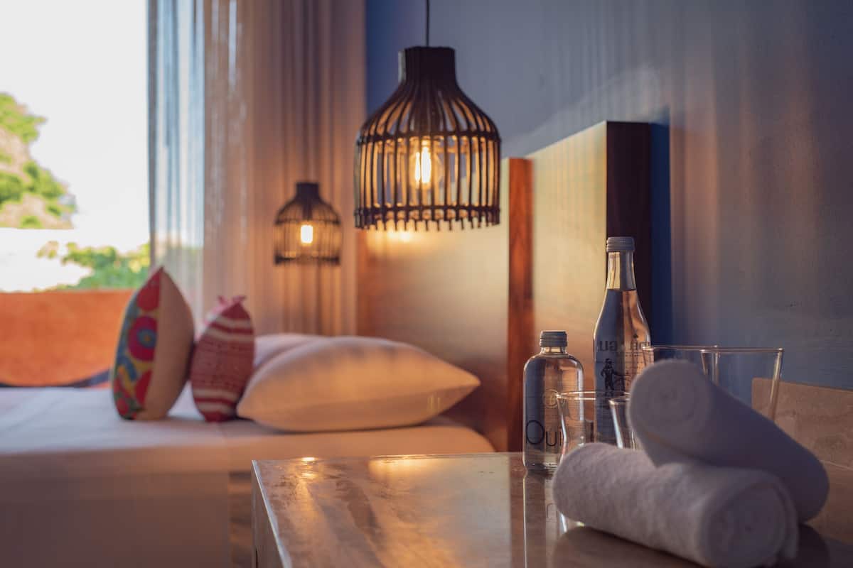 A room with a bed, a table with a bottle and glasses, and hanging pendant lights.