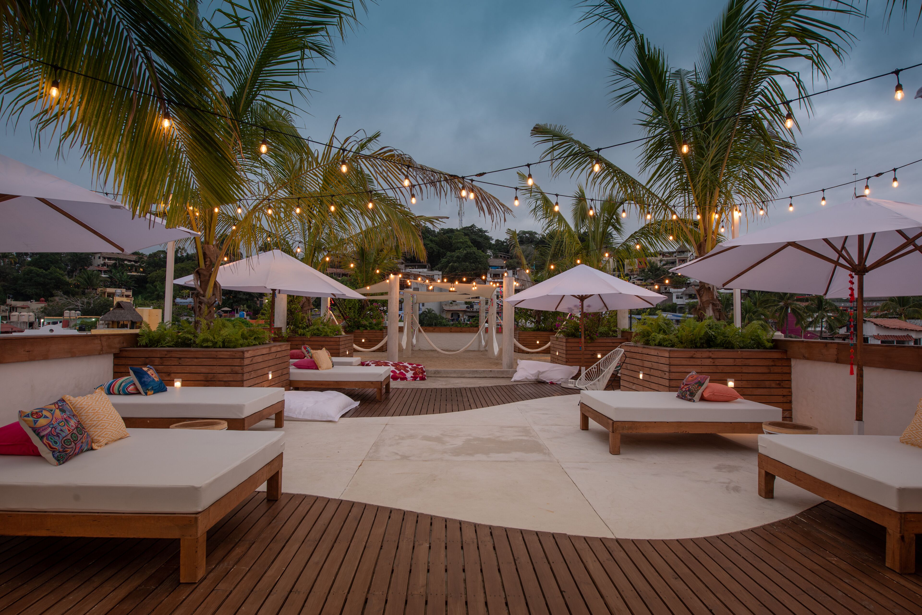 An outdoor lounge area with wooden flooring, white lounge chairs, and umbrellas.