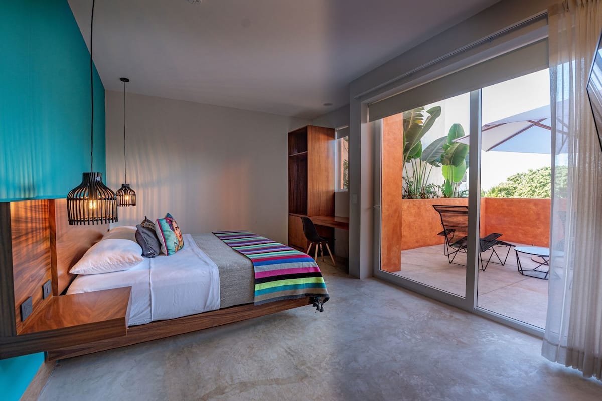 A bedroom with a bed, desk, and a view of an outdoor patio.