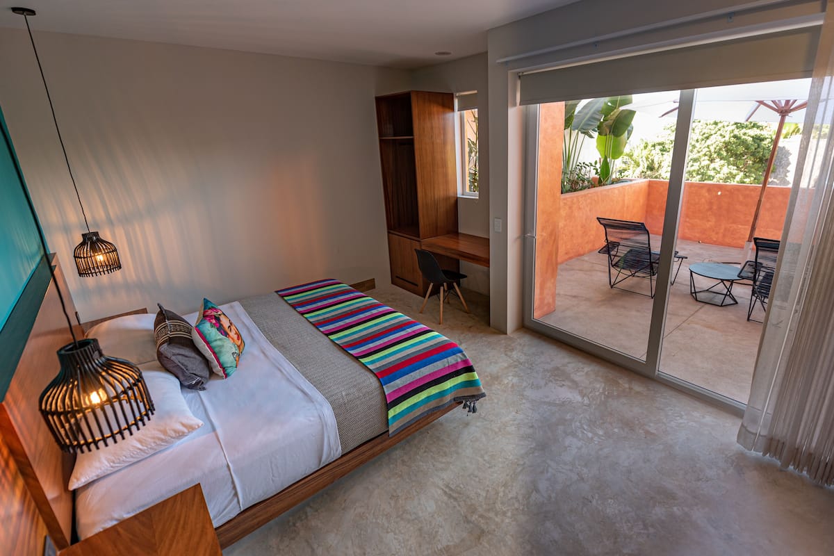 A bedroom with a bed, a desk, and a view of the outdoor patio.