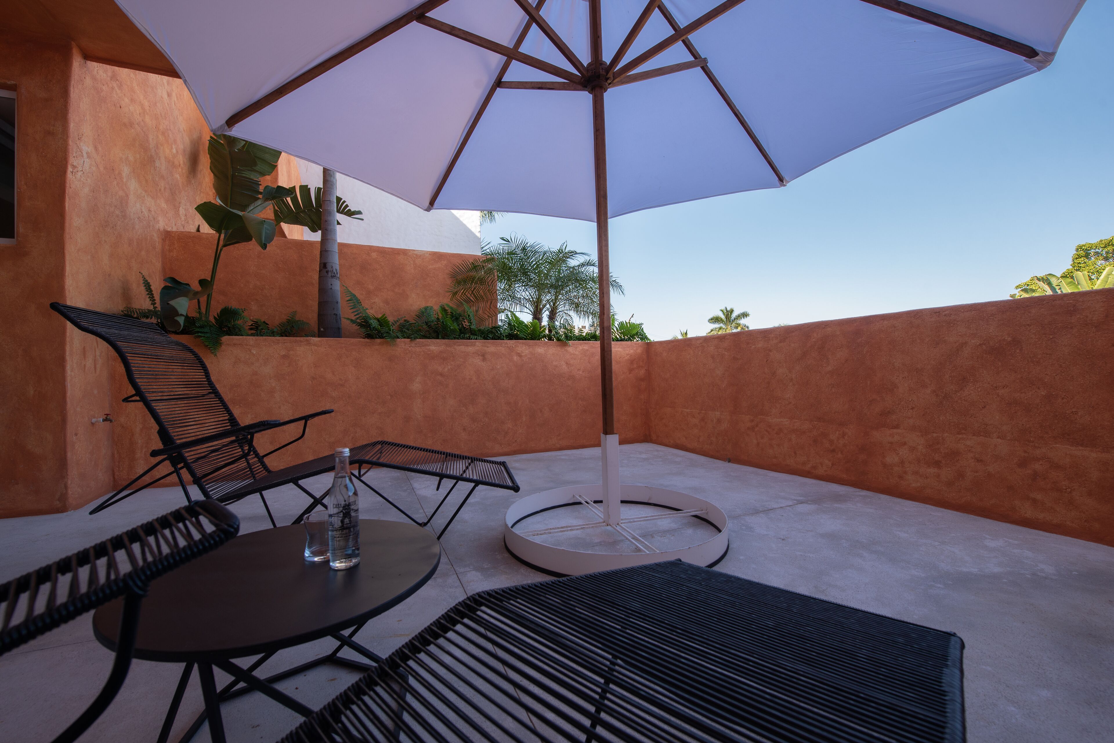 An outdoor patio with a round table, two chairs, a large umbrella, and a bottle of water.