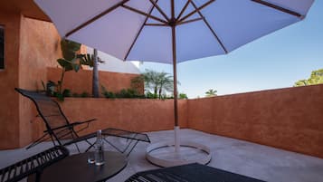 An outdoor patio with a round table, two chairs, a large umbrella, and a bottle of water.