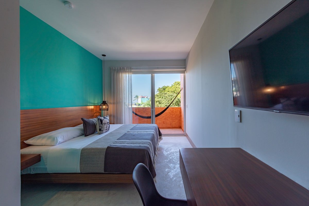 A hotel room with a bed, a desk, a TV, and a view of the outdoors.