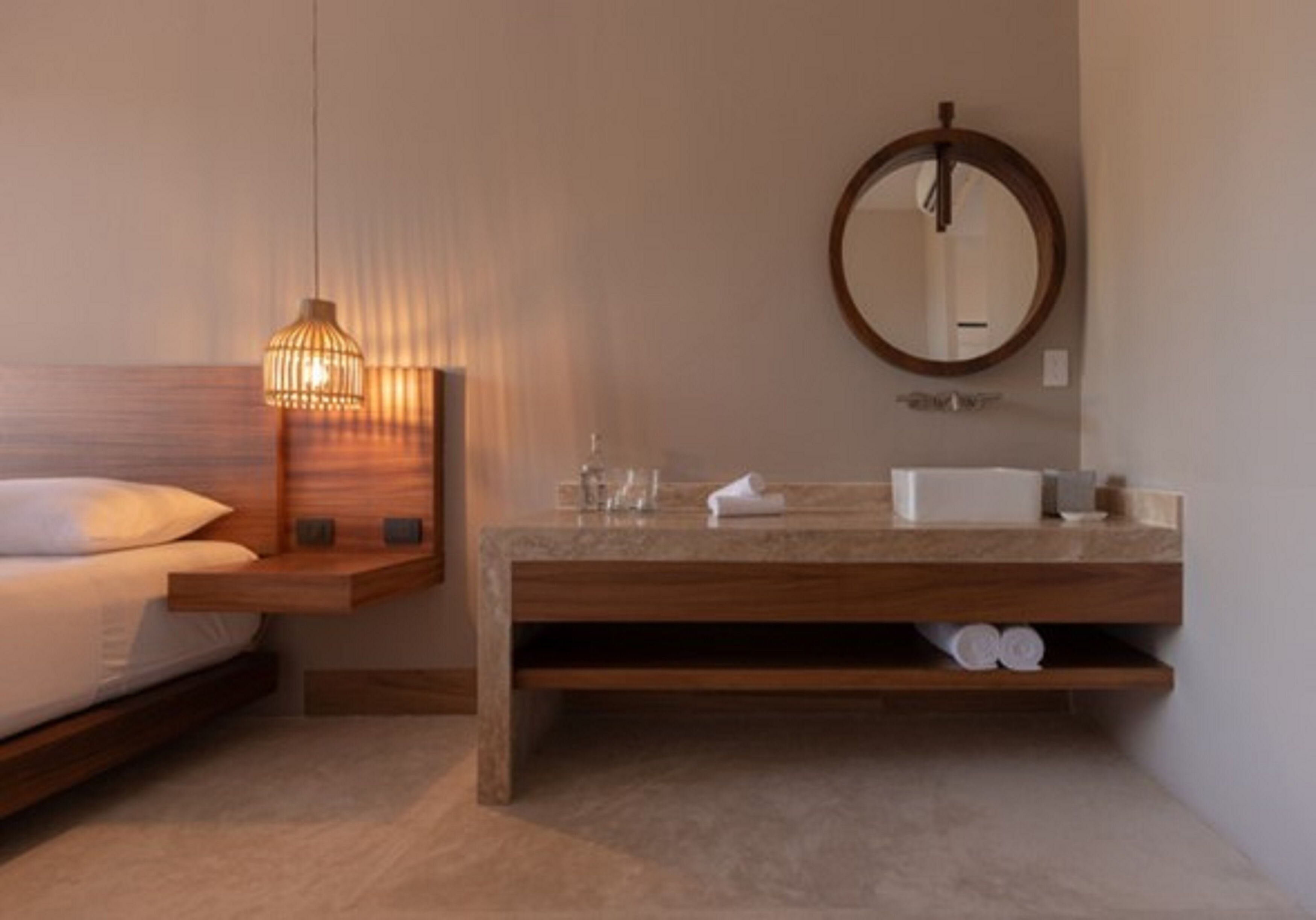 A modern bathroom with a wooden vanity, a round mirror, and a bedside lamp.