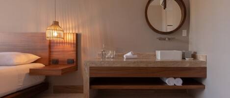 A modern bathroom with a wooden vanity, a round mirror, and a bedside lamp.