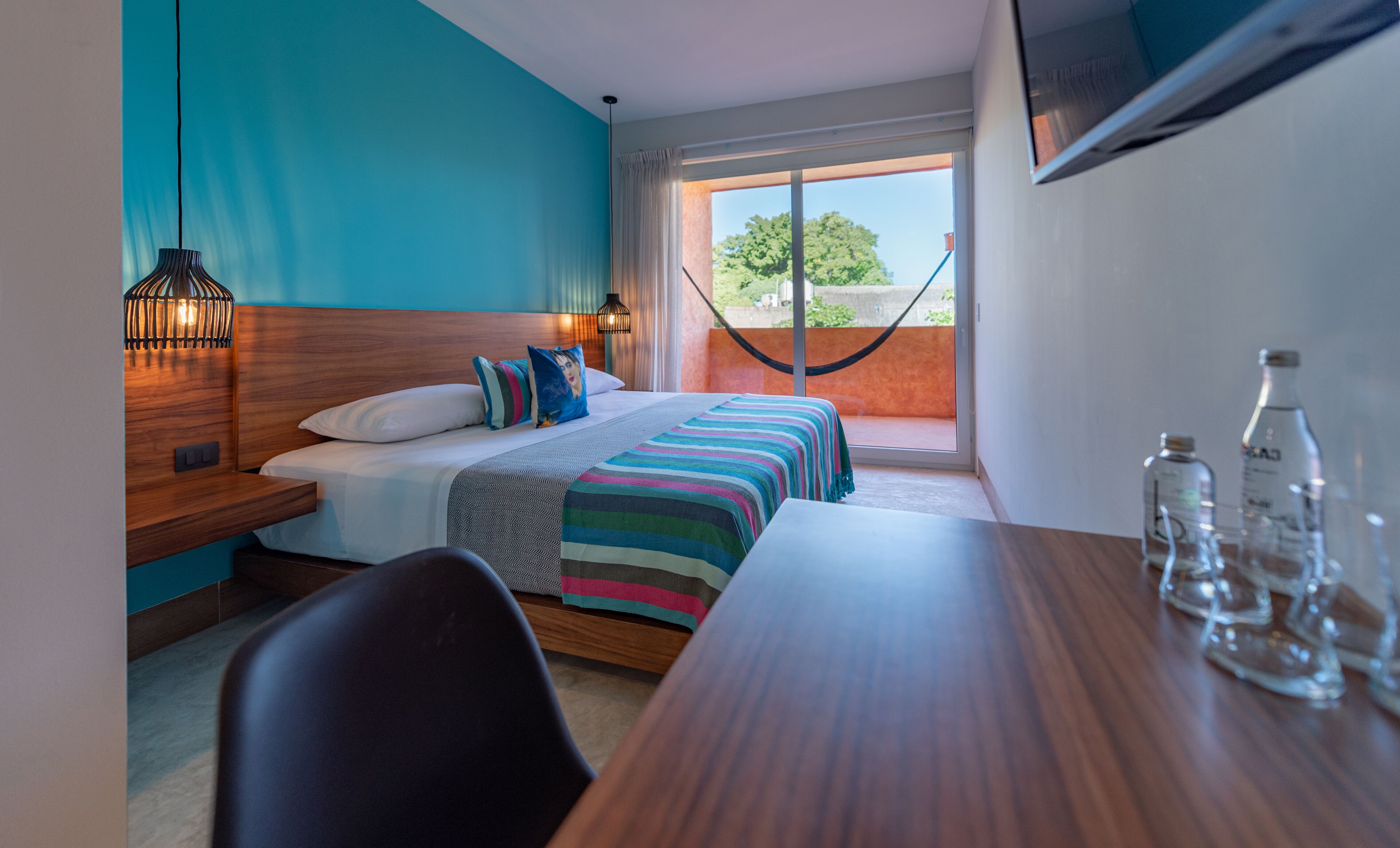 A hotel room with a bed, bedside table, chair, and a window with a view of greenery.
