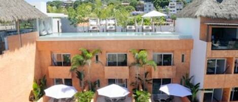 Un hotel con piscina en la azotea, varios balcones y mobiliario exterior con sombrillas.
