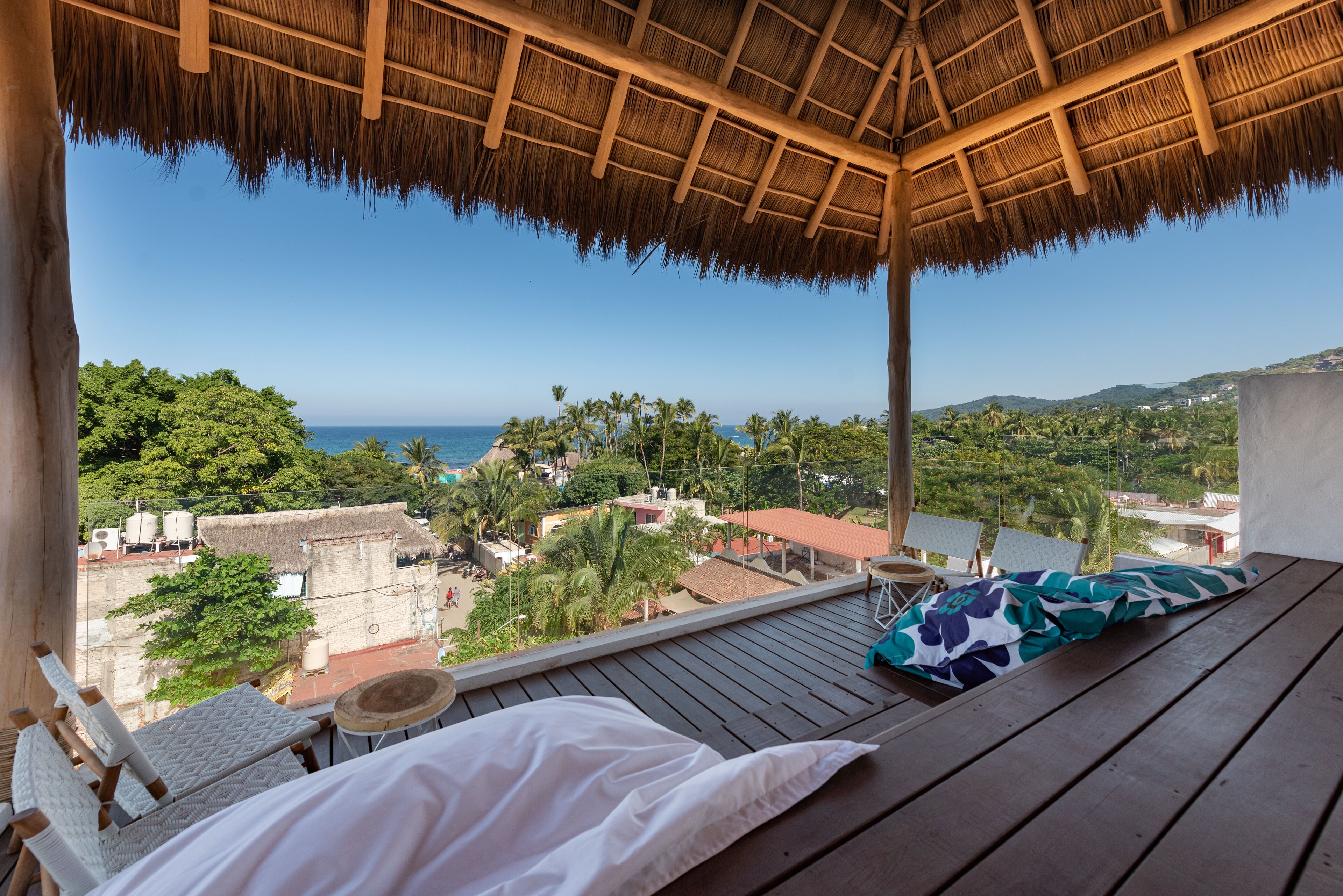 Ein Balkon mit einem Reetdach, der auf eine Küstenlandschaft mit Meer und üppiger Vegetation blickt.