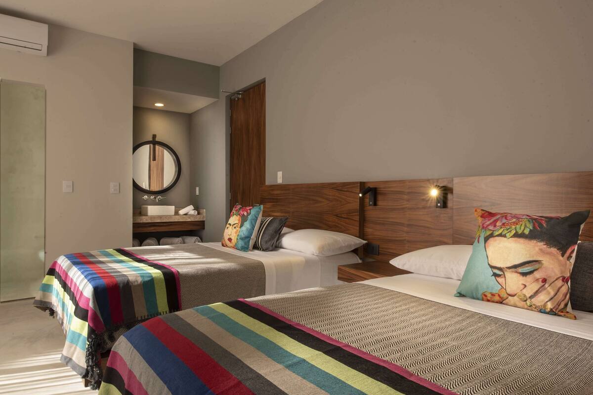 A hotel room with two beds, a wooden headboard, a mirror, a bathroom with a sink, and a shower area.