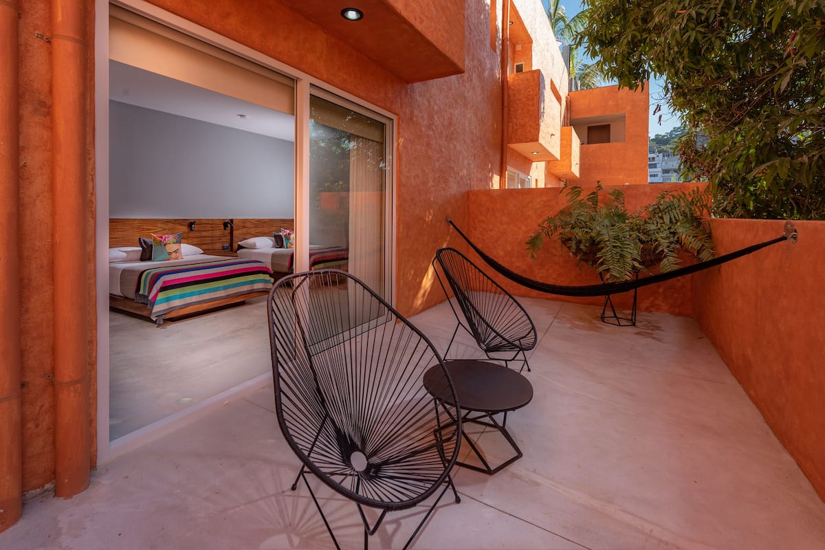 A modern hotel room with a large sliding glass door leading to a balcony, two black wireframe chairs, and a small table.