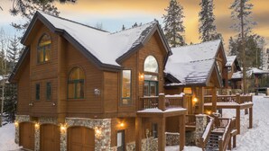 A wooden cabin with a stone foundation, multiple garage doors, and a covered porch with a staircase. - Walking distance to downtown Breck, Stunning ski resort panorama, hot tub, foosball, arcade machine! (Breckenridge)