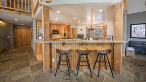 A spacious kitchen with wooden cabinets, a granite countertop, and three bar stools. - Walking distance to downtown Breck, Stunning ski resort panorama, hot tub, foosball, arcade machine! (Breckenridge)