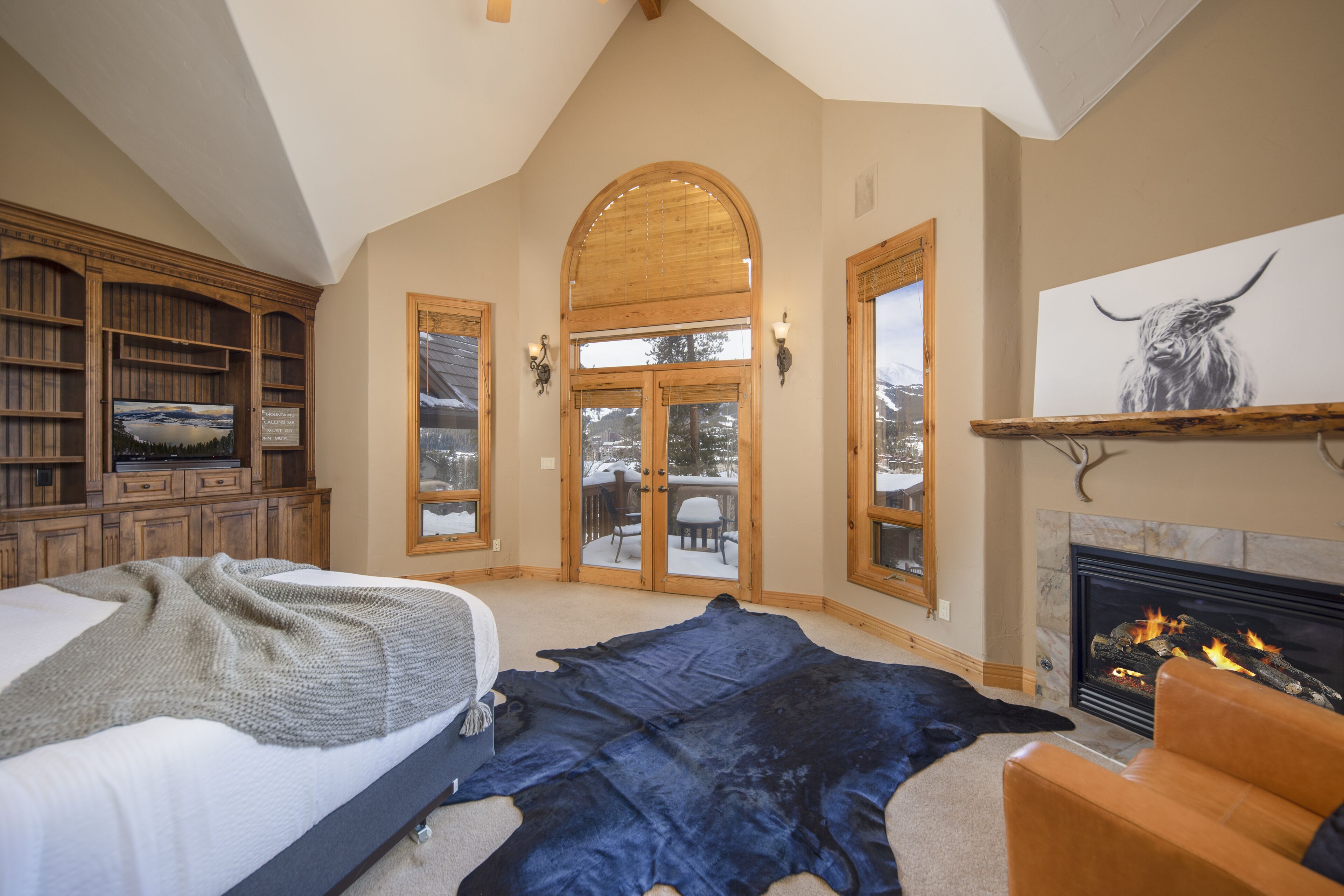 Een ruime kamer met een groot bed, een open haard, een houten boekenkast en een groot raam met uitzicht op een besneeuwde veranda.