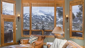 A cozy room with large windows offering a view of a snowy mountain landscape. - Walking distance to downtown Breck, Stunning ski resort panorama, hot tub, foosball, arcade machine! (Breckenridge)